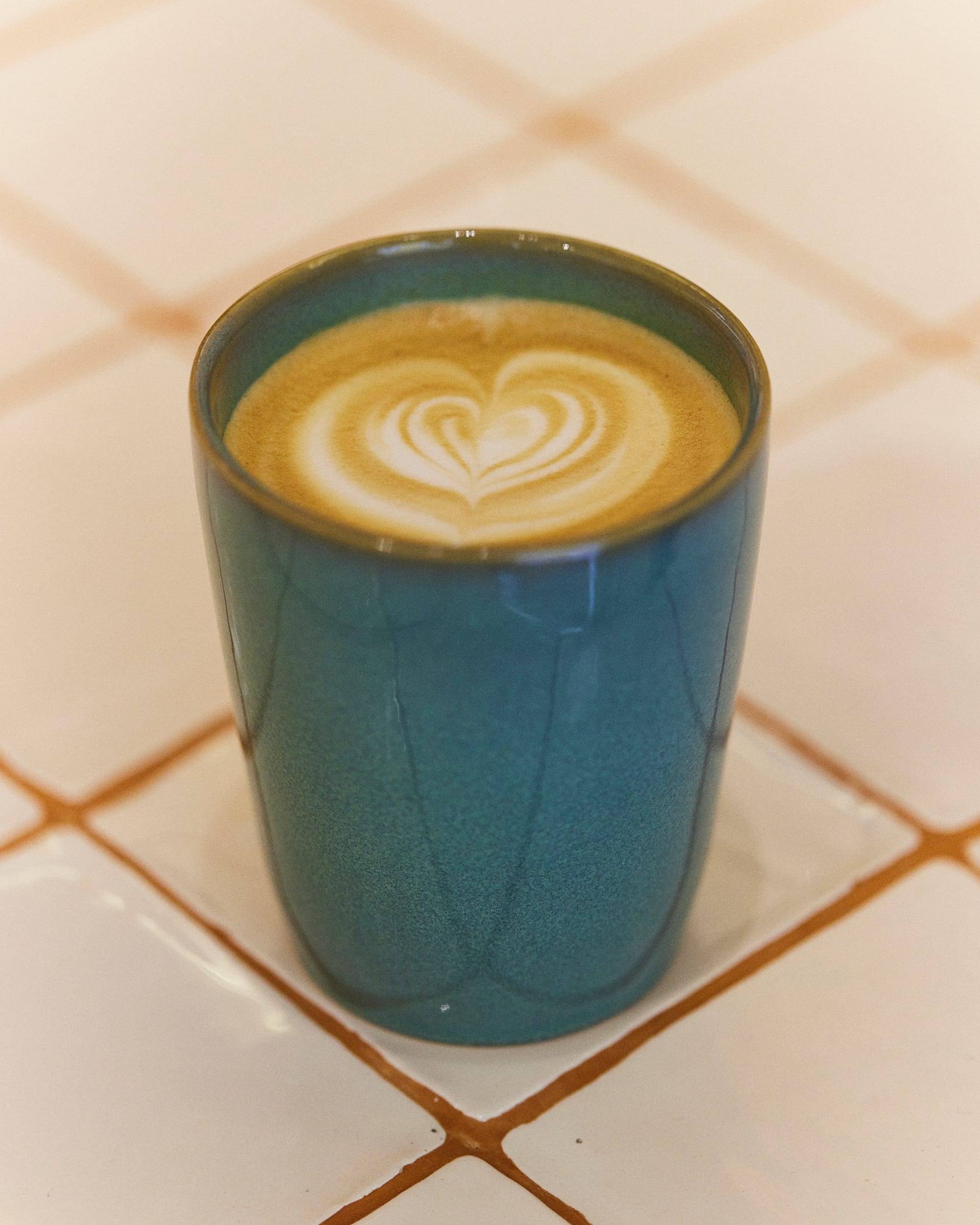 Petrol-teal cup seen from above with latte art, on pale tile