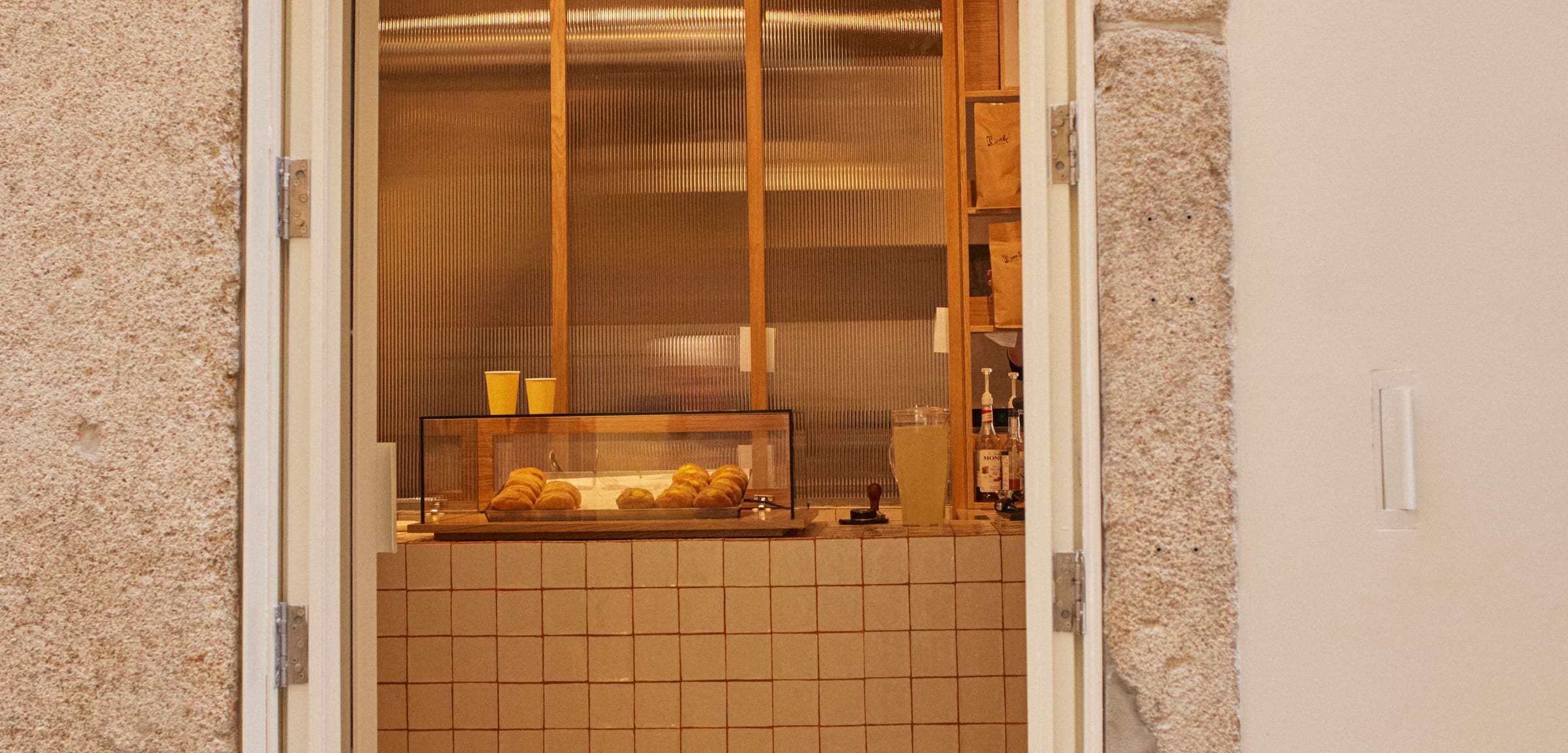 View through the granite doorway: the glass case of bolas de Berlim and the warmly lit tiled counter