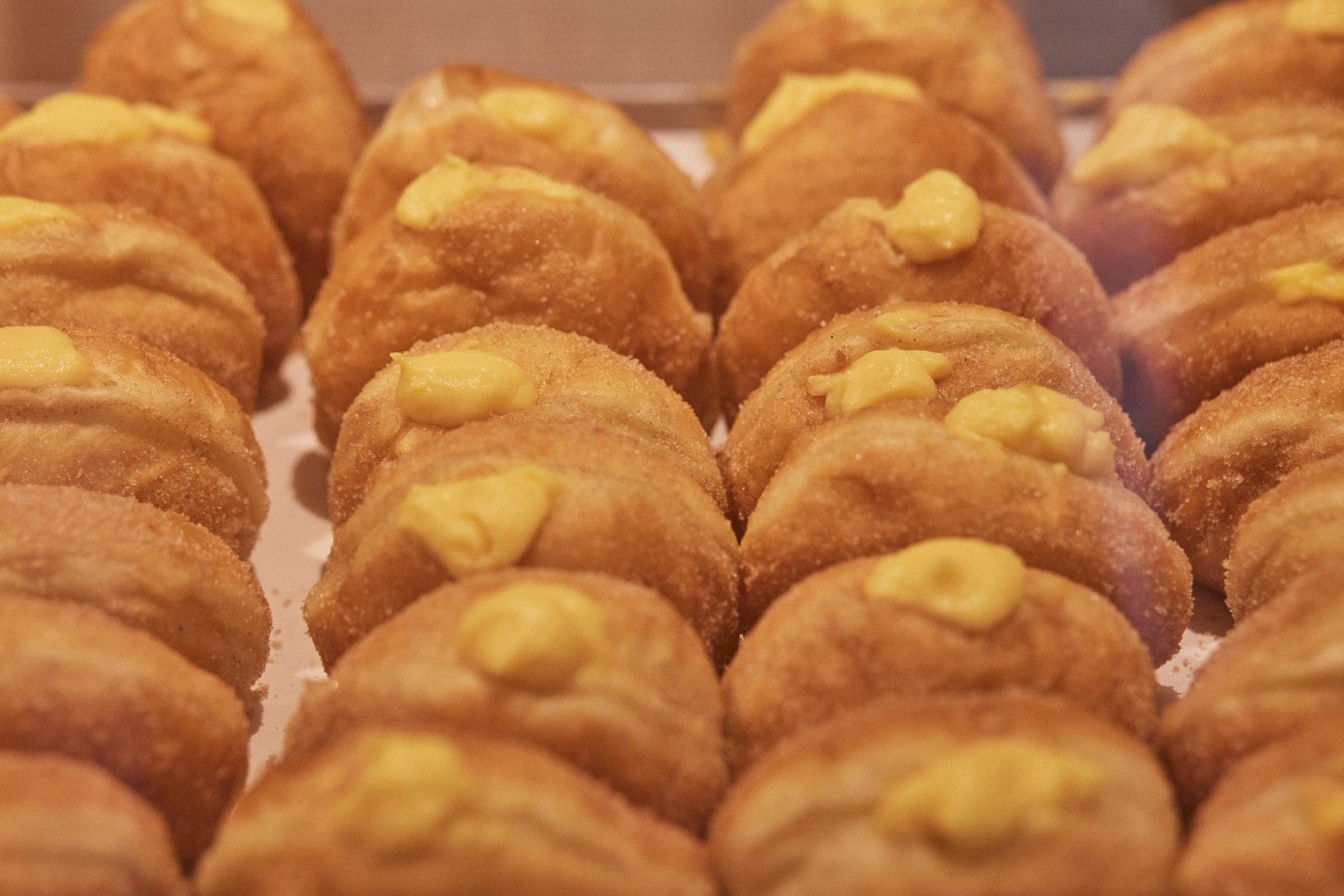 Close-up tray of sugar-rolled bolas de Berlim, rows deep, custard piped visibly on top